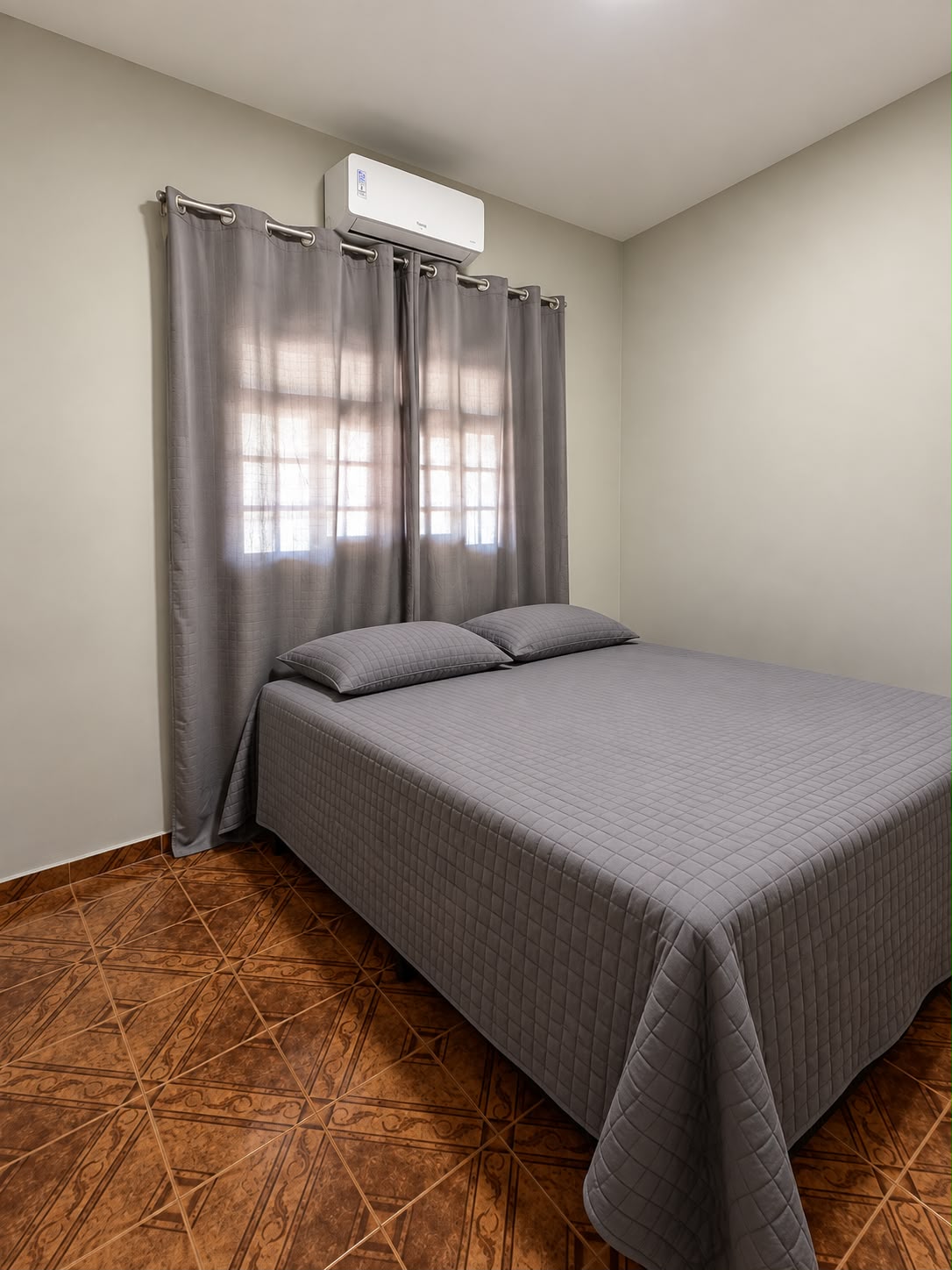 Quarto com cama de casal, parede clara e janela com cortinas